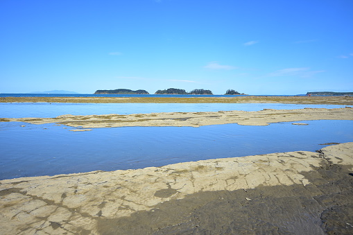 Flat coast with rocky platforms drying during periods of low tide with small forest covered islands in far background.