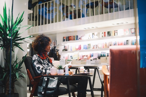 Young woman reading a book and having a hot tea in the bookstore cafe.