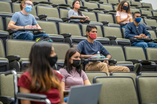 University students wearing masks in a lecture hall College students sitting in a lecture hall keeping social distance during the COVID-19 pandemic and wearing masks to protect from the transfer of germs. community college stock pictures, royalty-free photos & images