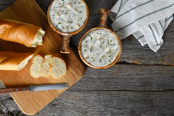 Top view of two bowls of homemade Clam Chowder with fresh baked loaf of bread. Horizontal with copy space.