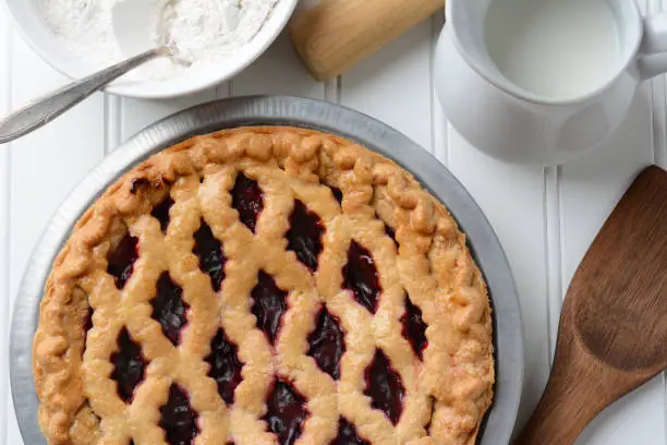 High angle shot of a fresh baked fruit pie with a lattice crust. the pie is surrounded by baking items. Horizontal format.