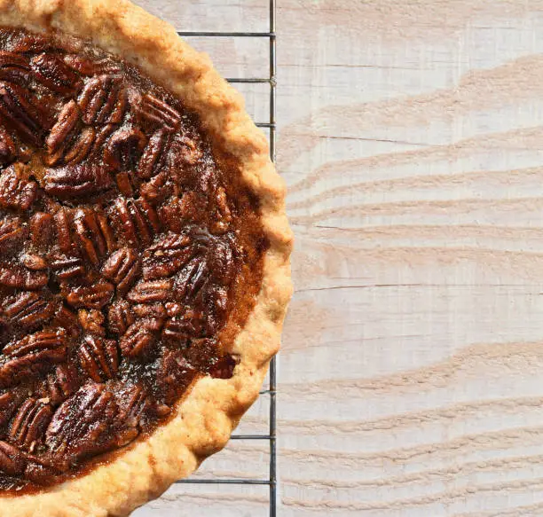High angle view of a fresh baked holiday Pecan Pie on a cooling rack atop a rustic wood kitchen table. Only half the pie is shown leaving copy space.