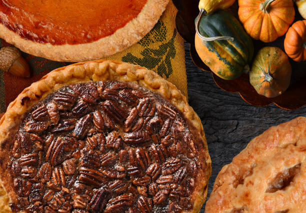 Thanksgiving Holiday Pecan , Pumpkin, and Apple Pies on a rustic table with decorative gourds.