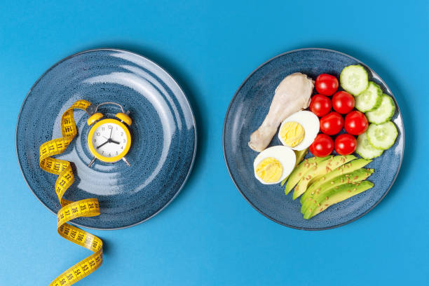 comida e despertador em fundo azul, conceito de jejum intermitente. - plate blue loss tape measure - fotografias e filmes do acervo