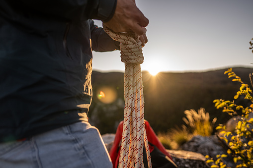 Man holding and packing climbing rope after abseil in nature during sunset, close up