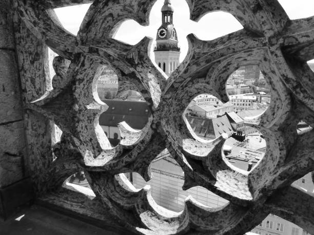 Close-up View of the intricate gothic stonework at the top of the Marienplatz Clock tower. Steeple of St Peter's Church can be seen in the background