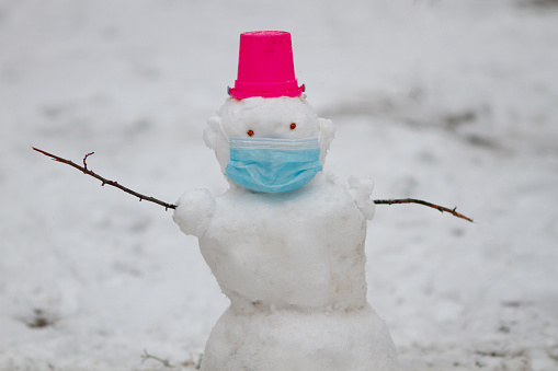 Snowman wearing protection mask standing outdoors on playground on a snowy winter day. Covis protection concept. New normal
