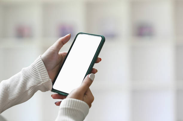 istock A mock up smartphone blank screen in female hands with blurred office interior background. 1282775702