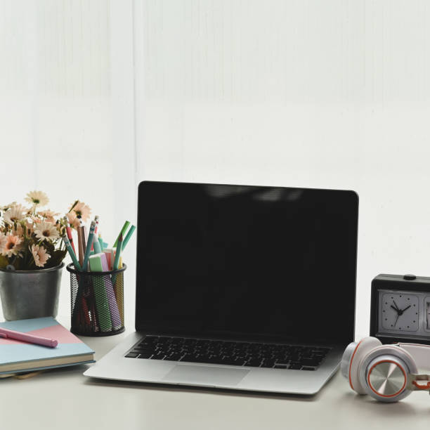 istock Simple workspace with blank screen laptop, notebooks, headphone, clock and tree pot on white table. 1282775705