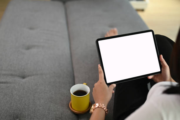 istock Mockup image of female hand holding tablet with blank white screen  while sitting on couch at home. 1282775730
