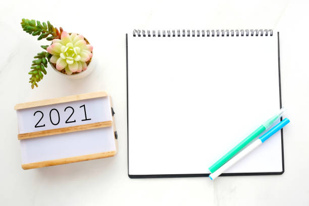 istock 2021 on wood box, blank notebook paper on white marble table background, 2021 new year mock up, template with copy space for text, top view 1282781479