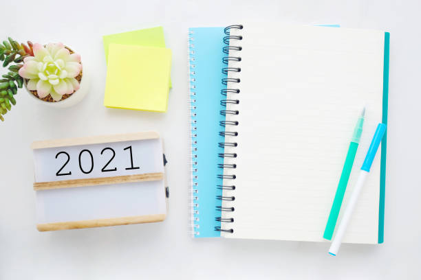 istock 2021 on wood box, blank notebook paper on white marble table background, 2021 new year mock up, template with copy space for text, top view 1282781505