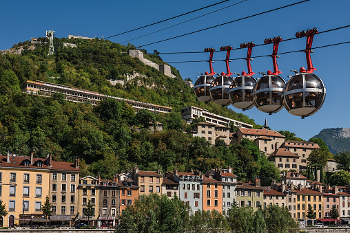 Grenoble, France - august 12, 2018. Closeup view of Grenoble cable way with moving gondolas by summer day. Isere river, French alps, colorful old town buildings, fortress, Bastille and cable cars.