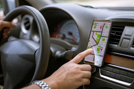 Male driver searching location using GPS navigation in mobile phone before driving car.