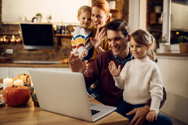 Happy family using laptop and making video call on Thanksgiving at home. Happy parents and kids waving while having video call over laptop on Thanksgiving at home. thanksgiving holiday covid stock pictures, royalty-free photos & images