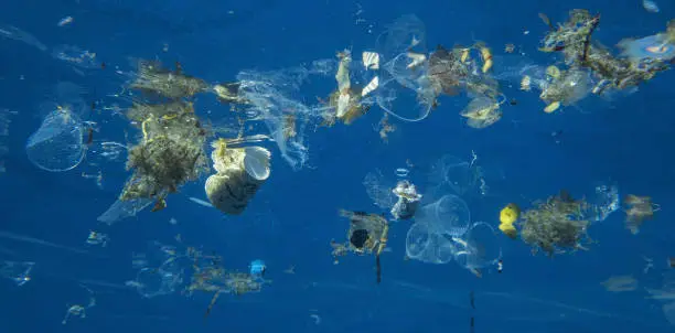 Photo of Plastic and other debris floats underwater in blue water. Plastic garbage polluting seas and ocean