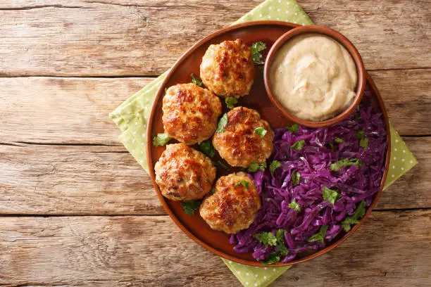 Photo of Frikadeller or Danish Meatballs are savory meatballs served with rich creamy sauce and stew red cabbage close up in the plate. horizontal top view