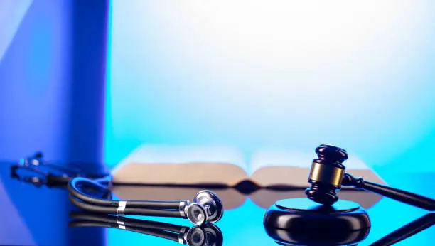 Gavel, legal code and stethoscope on the glass table. Blue light.