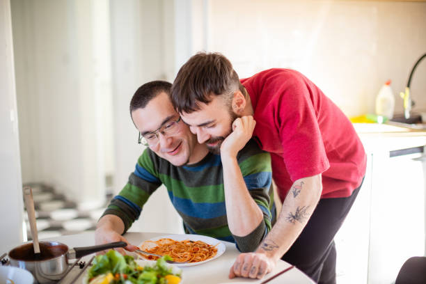 istock Young man eating spaghetti at the table, his boyfriend leaning on him from behind 1282800809