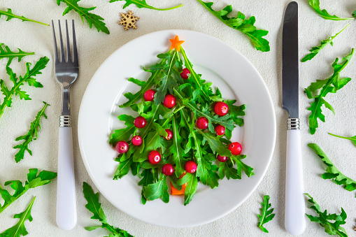 The Christmas tree arugula salad on white plate with knife and fork. Vegetarian concept. Flat lay