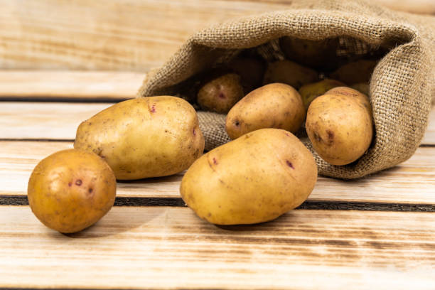 istock Fresh potatoes in an old bag on a wooden background. 1282806977