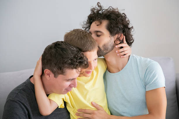 Two happy handsome dads hugging and kissing son Two happy handsome dads hugging and kissing son, enjoying leisure time together. Happy family and gay parents concept gay daddy stock pictures, royalty-free photos & images