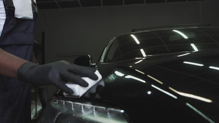 An African-American service worker applies a protective layer. Applying protection for headlights. Professional Car Ceramics Worker applies a layer of ceramics protective rain cover on car windows. Concept from Nano Protection, Different accessories, Long