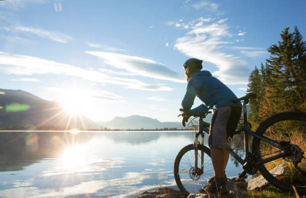 Mountain biker relaxes by lakeshore at sunrise Sun rises over distant coastline canadian rockies photos stock pictures, royalty-free photos & images
