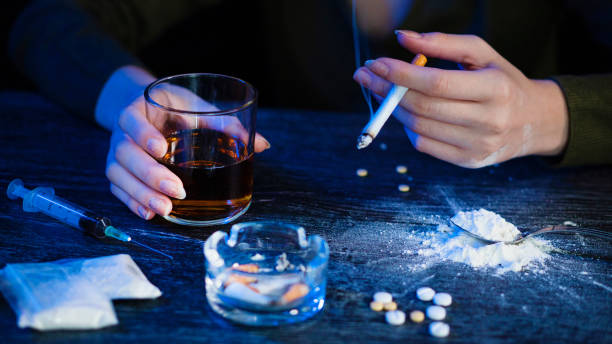 giovane donna che tiene in mano una sigaretta e whisky con eroina, siringa, pillole, droghe, posacenere sul tavolo marrone in legno. - narcotic teenager marijuana drug abuse foto e immagini stock