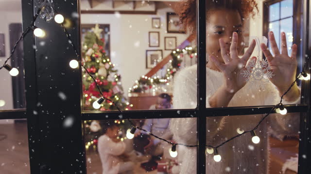 Happy girl decorating snowflake at the window while first Snow falling, winter and Christmas scene concept