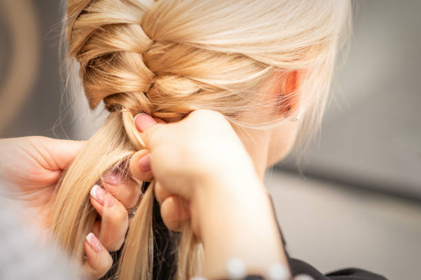 Female hands braiding pigtail to woman Close up back view of female hands braiding a pigtail to young blond woman at beauty salon Pigtails stock pictures, royalty-free photos & images