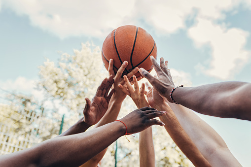 multi-ethnic sports group raising arms holding basketball