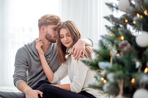 Happy couple in love celebrating Christmas together at home next to Xmas tree