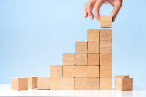 istock Businessman hand Arranging Wood Block Stacking as Step Stair on blue background 1282819101