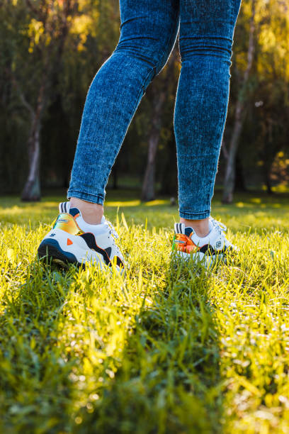 istock White sneakers with black inserts on female legs dressed in jeans on green grass 1282825040