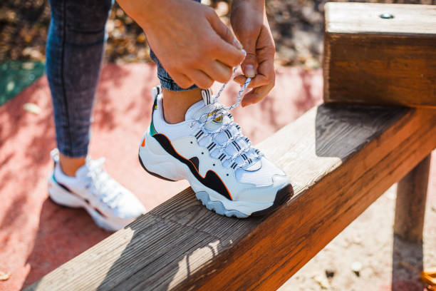 Female hands tying laces on white sneakers with black inserts standing on a wooden parapet Female hands tying laces on white sneakers with black inserts standing on a wooden parapet lace up stock pictures, royalty-free photos & images