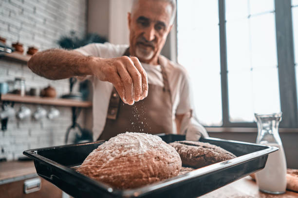 Mature chef holding oven-tray with baked bread at home Adult bearded man using flour while making homemade bread in the kitchen. Baking process concept. Copy space baking bread photos stock pictures, royalty-free photos & images