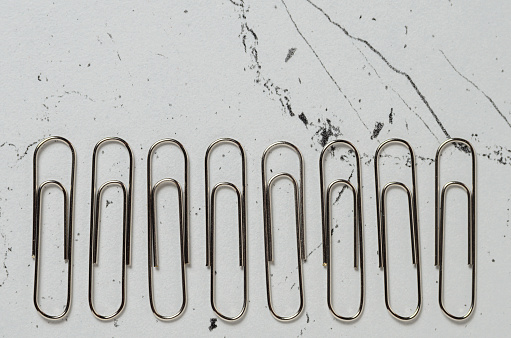 Office supplies, Nickel-plated paper clips on the textured surface of the table. Selective focus.