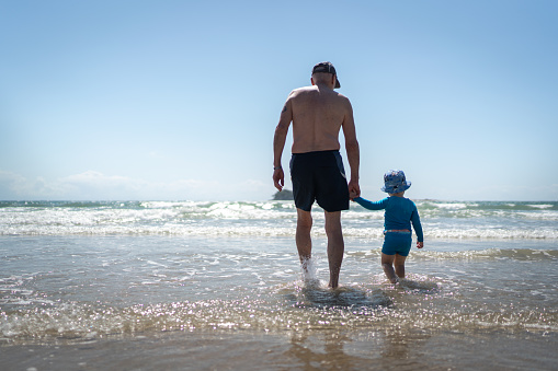 Rear view of baby boy entering into the sea with grandfather