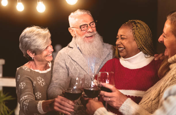 amigos veteranos felizes celebrando feriados enquanto brindam com taças de vinho tinto na festa do pátio da casa - férias e festejos - fotografias e filmes do acervo