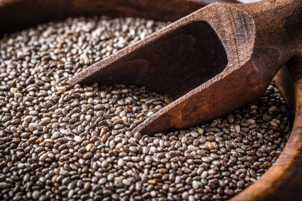 Top view of chia seeds background with an empty wooden serving scoop on right top corner leaving a useful copy space on the chia seeds background. Predominant color is brown. Studio shot taken with Canon EOS 6D Mark II and Canon EF 100 mm f/ 2.8