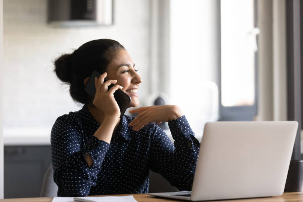 istock Smiling Indian woman talk on cellphone working on laptop 1282835185