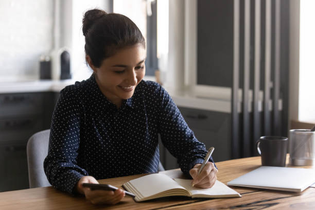 istock Smiling Indian woman write in notebook using cellphone 1282835198