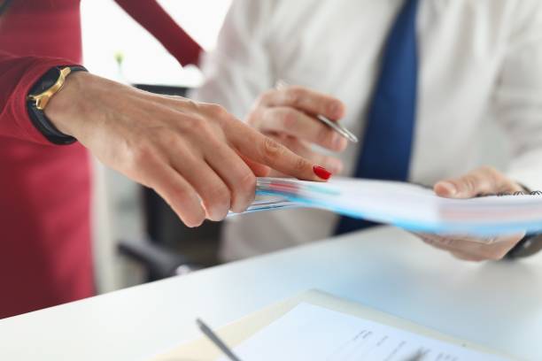 istock Man's hand holds notebook with pen next to a woman stands and points a finger. 1282836219