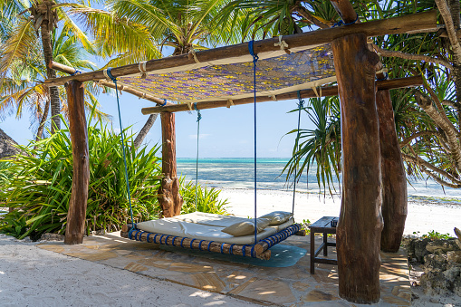 Wooden swing with a mattress and pillows under a canopy on the tropical beach near sea, island Zanzibar, Tanzania, East Africa