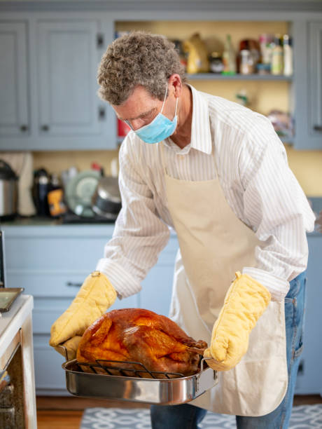 Mature Adult Man Cooking Thanksgiving Turkey Dinner Wearing COVID-19  PPE Face Mask Mature Adult Man Cooking Thanksgiving Turkey Dinner Wearing COVID-19  PPE Face Mask thanksgiving holiday covid stock pictures, royalty-free photos & images