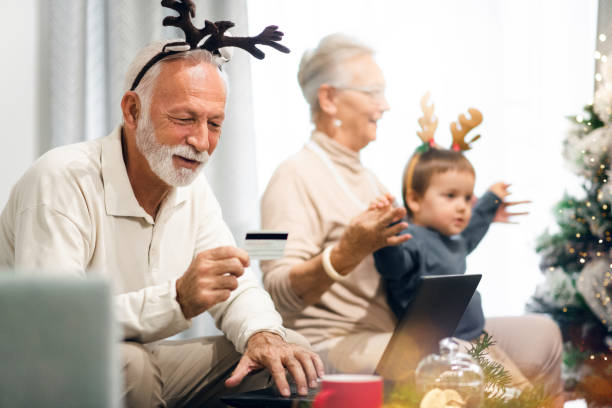 il nonno sta comprando online, mentre la nonna sta giocando con il nipote. concetto di natale. - christmas shopping internet family foto e immagini stock