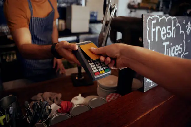 Photo of Female hands holding card against nfs payment machine to make payment for purchase in cafe