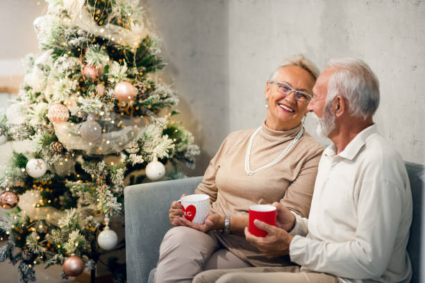 istock Senior married couple is sitting on sofa, drinking hot beverages. Christmas time. 1282847354