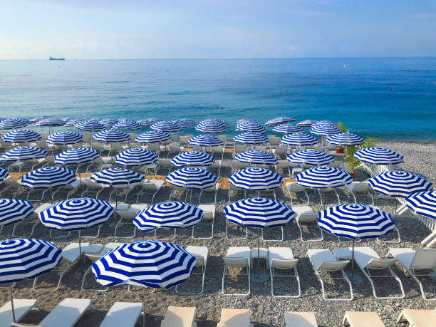 rating dAzur, France Nice stone beach and turquiose water of cote dAzur at summer morning with open traditional umbrellas, french riviera coast french riviera stock pictures, royalty-free photos & images